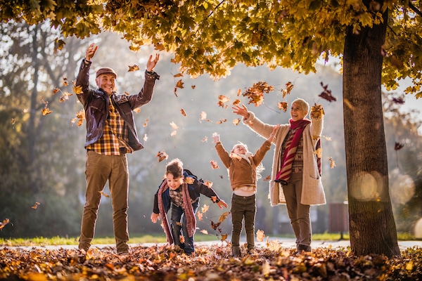 Playful grandparents and their grandkids having fun while throwing autumn leaves in the park