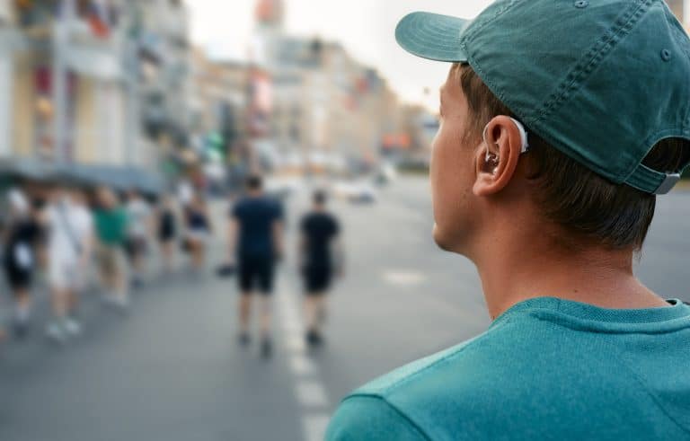 Young man with a hearing aid walking around a noisy city.
