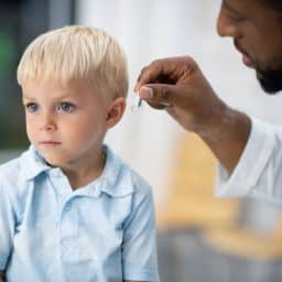 An audiologist fits a hearing aid on to a little boy.