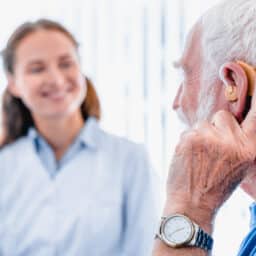 Focused picture of an elderly male patient with hearing aid side view with blurred woman doctor in the background