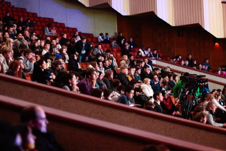 People sitting and watching a performance in a large theater.