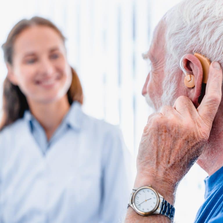a male patient with hearing aid side is pictured with an audiologist in the background
