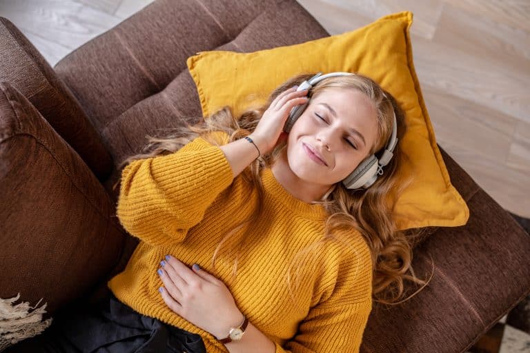 A woman lies on a couch listening to music with over-the-ear headphones