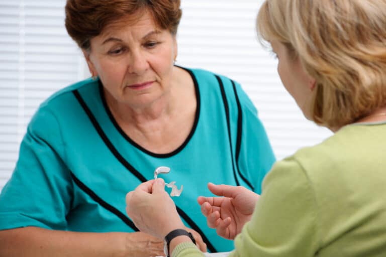Audiologist showing a hearing aid to a senior woman.