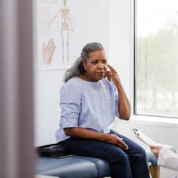 Woman pointing to her ear, talking to audiologist